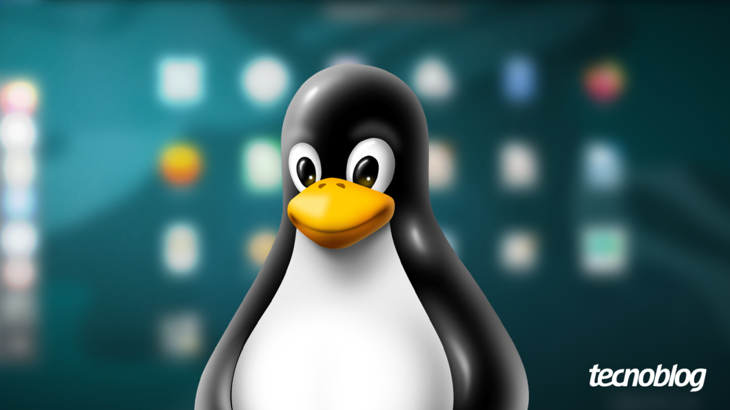 Imagem do Tux, o pinguim mascote do sistema operacional Linux. O pinguim preto e branco, com bico amarelo e olhar amigável, está centralizado em primeiro plano. O fundo está desfocado e exibe o que parece ser uma tela de área de trabalho de computador. O logo do "Tecnoblog" aparece no canto inferior direito.