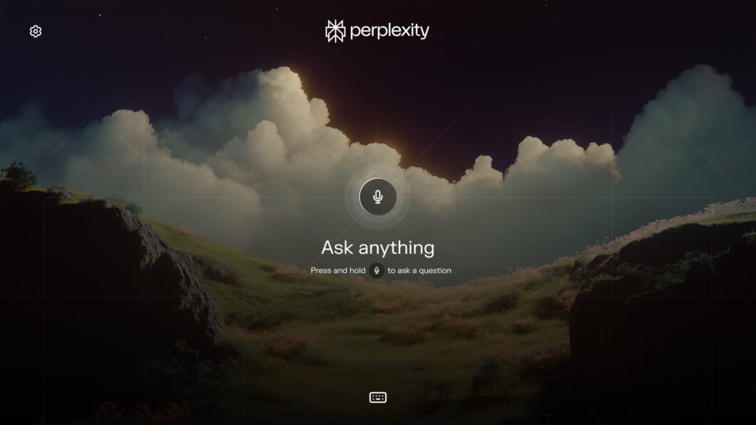 Captura de tela da interface do aplicativo Perplexity para TV, com um tema visual noturno ou crepuscular que apresenta colinas gramadas, céu dramático com grandes nuvens iluminadas e escuras. O centro da tela exibe um ícone de microfone e o texto 'Ask anything', indicando um recurso de busca por voz. O logotipo da Perplexity está no centro superior e um ícone de configurações no canto superior esquerdo.
