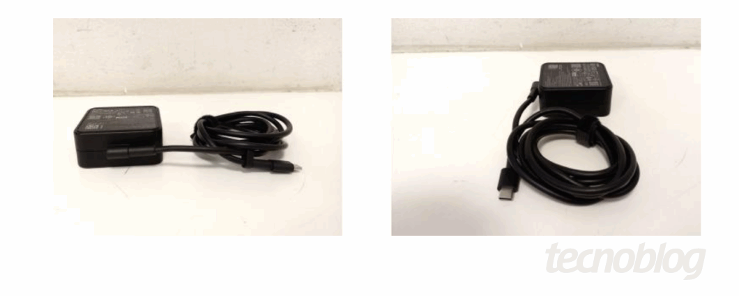 Imagem mostra um carregador preto sobre uma mesa branca. Na parte inferior direita, o logo do "tecnoblog"