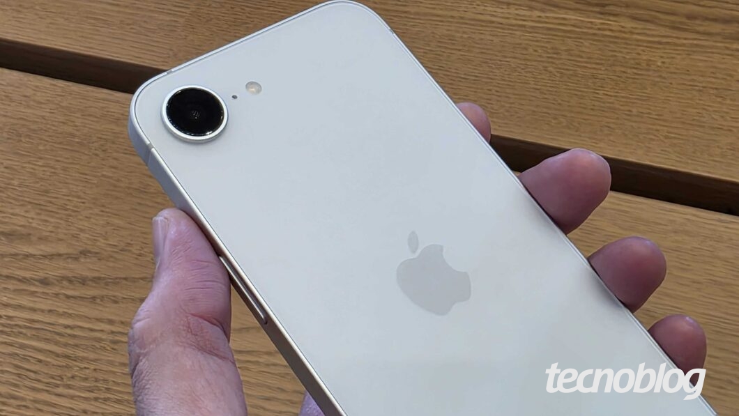 Imagem mostra um iPhone 16e sendo segurado em uma mão. A parte traseira está para cima.