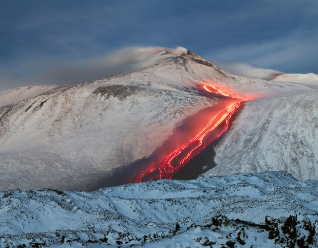 Lava flowing down the side of a snow-covered volcano 