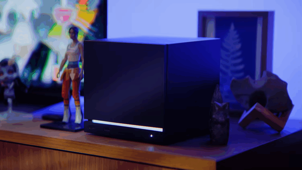 Imagem exibe uma Steam Machina sobre uma mesa de madeira. Se trata de um cubo preto, com um led branco na parte inferior.