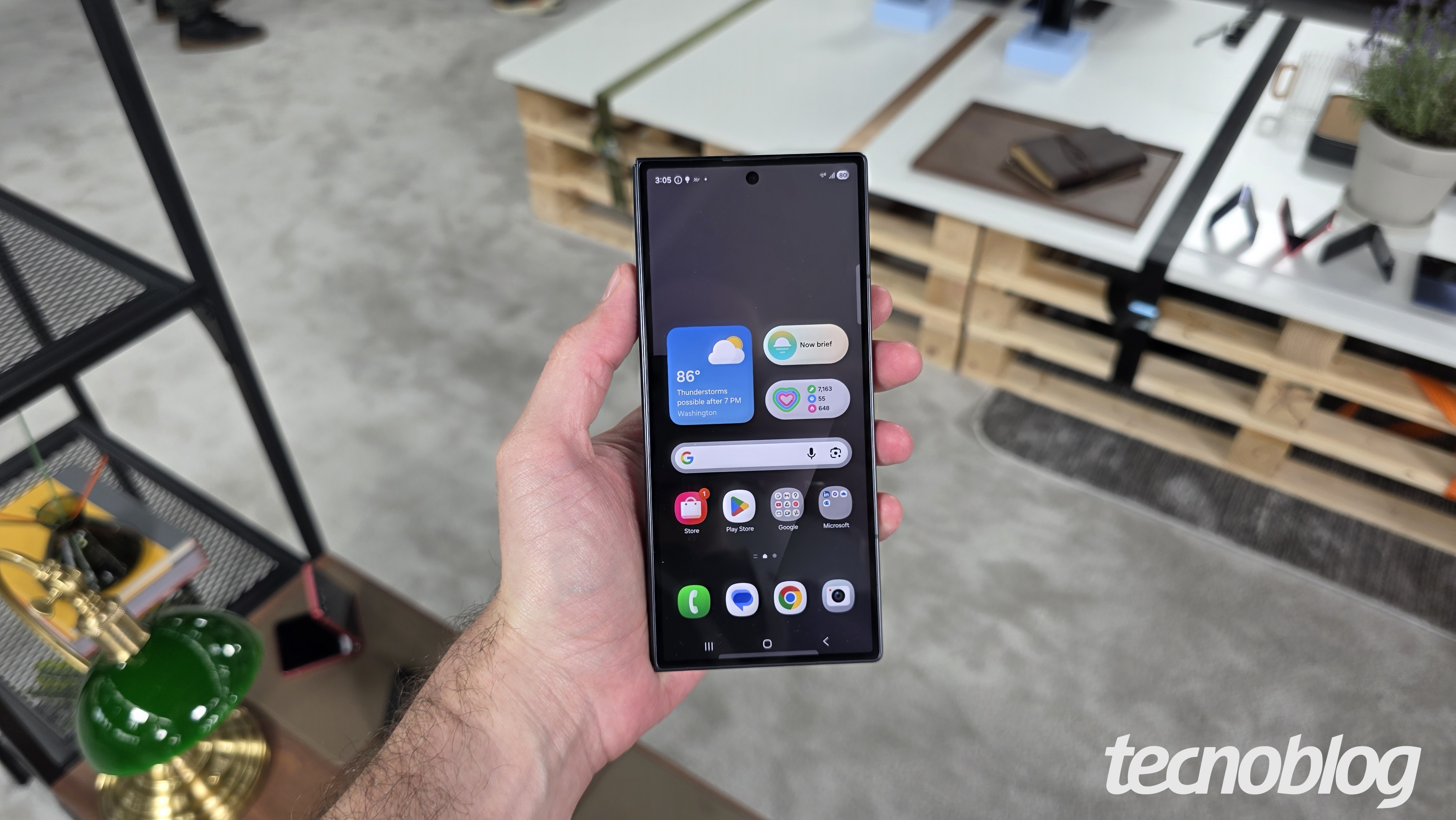 Mão segurando smartphone dobrável fechado, exibindo a tela inicial da One UI
