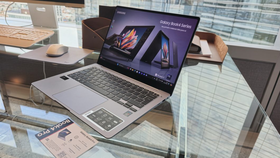 Notebook da série Galaxy Book4 da Samsung, aberto, em cima de uma mesa de vidro, acompanhado de mouse e teclado ao fundo