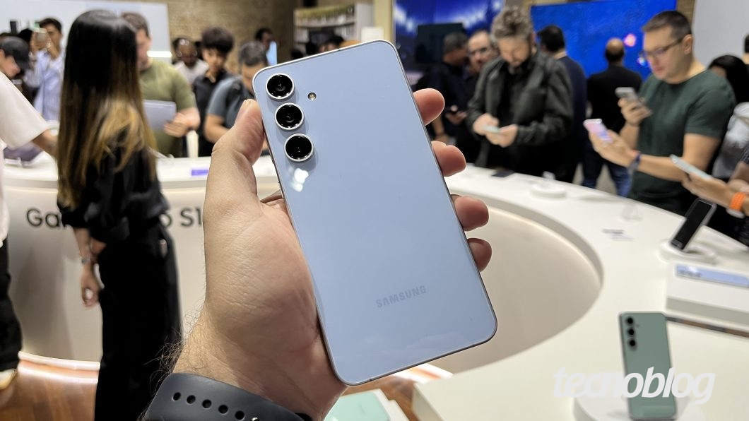 Mão esquerda segurando Galaxy S24 FE com a parte traseira voltada para a pessoa