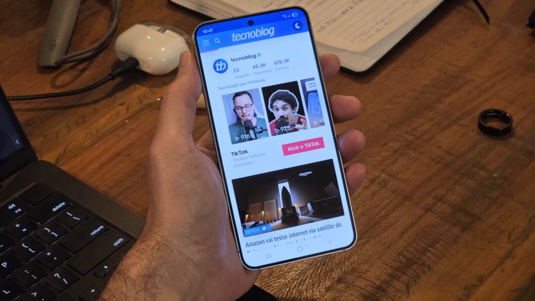Mão segurando Galaxy S25 com tela ligada mostrando perfil do Tecnoblog no TikTok
