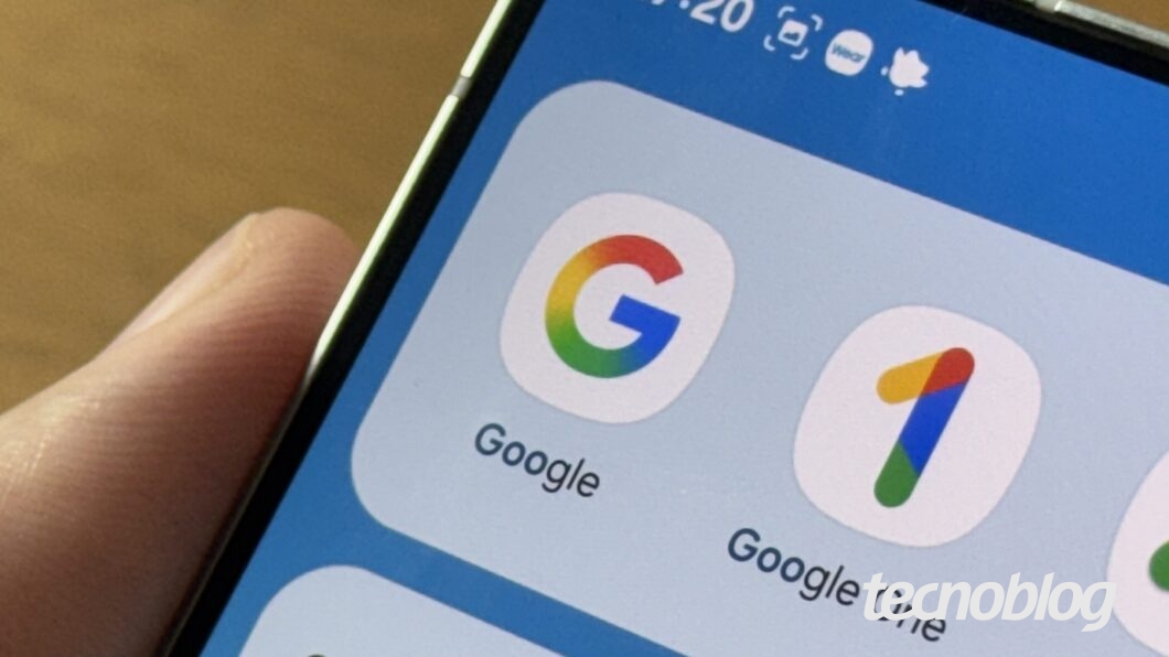 A imagem mostra a tela de um smartphone sendo segurado por uma mão. Na parte superior da tela, é possível ver a hora "17:20" e ícones de notificação. Abaixo, há três ícones de aplicativos: o logo colorido do Google, o ícone do Google One e o ícone do Google Ads, todos com design simples e minimalista. A interface do sistema está em um fundo azul claro. A mão que segura o dispositivo está posicionada na lateral.