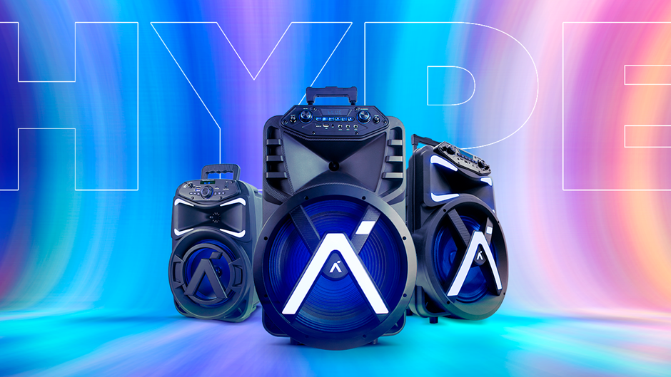 Três caixas de som de festa (party boxes) da marca Aquario em tamanhos diferentes, dispostas em um estúdio com iluminação de fundo em gradiente vibrante de azul, roxo e rosa. O modelo de caixa de som central e maior exibe um logo 'A' iluminado em branco neon no centro do woofer. O texto estilizado "HYPE" está sobreposto na imagem.