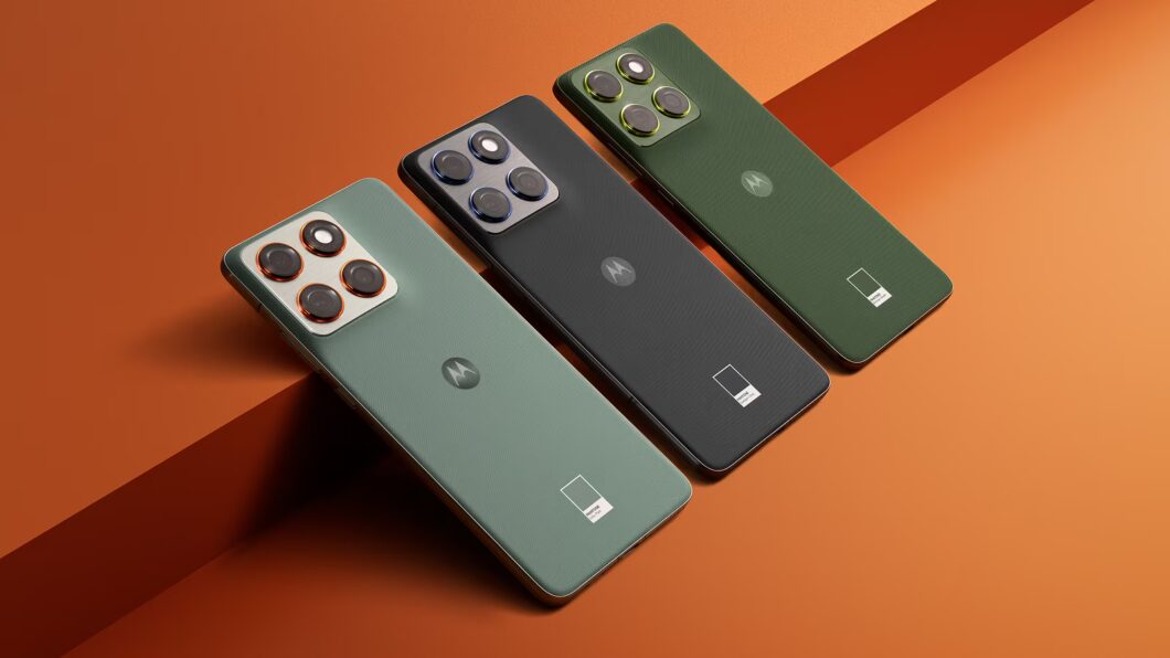 Ângulo superior de três smartphones Motorola Edge alinhados diagonalmente sobre um fundo em tom Laranja Queimado. As cores dos telefones são, da frente para trás: Verde Sálvia/Cinzento com anéis de câmera laranja-cobre; Cinza Escuro com anéis azuis; e Verde Floresta Escuro com anéis amarelo-esverdeados, cada um com o logo da Pantone na parte inferior traseira.