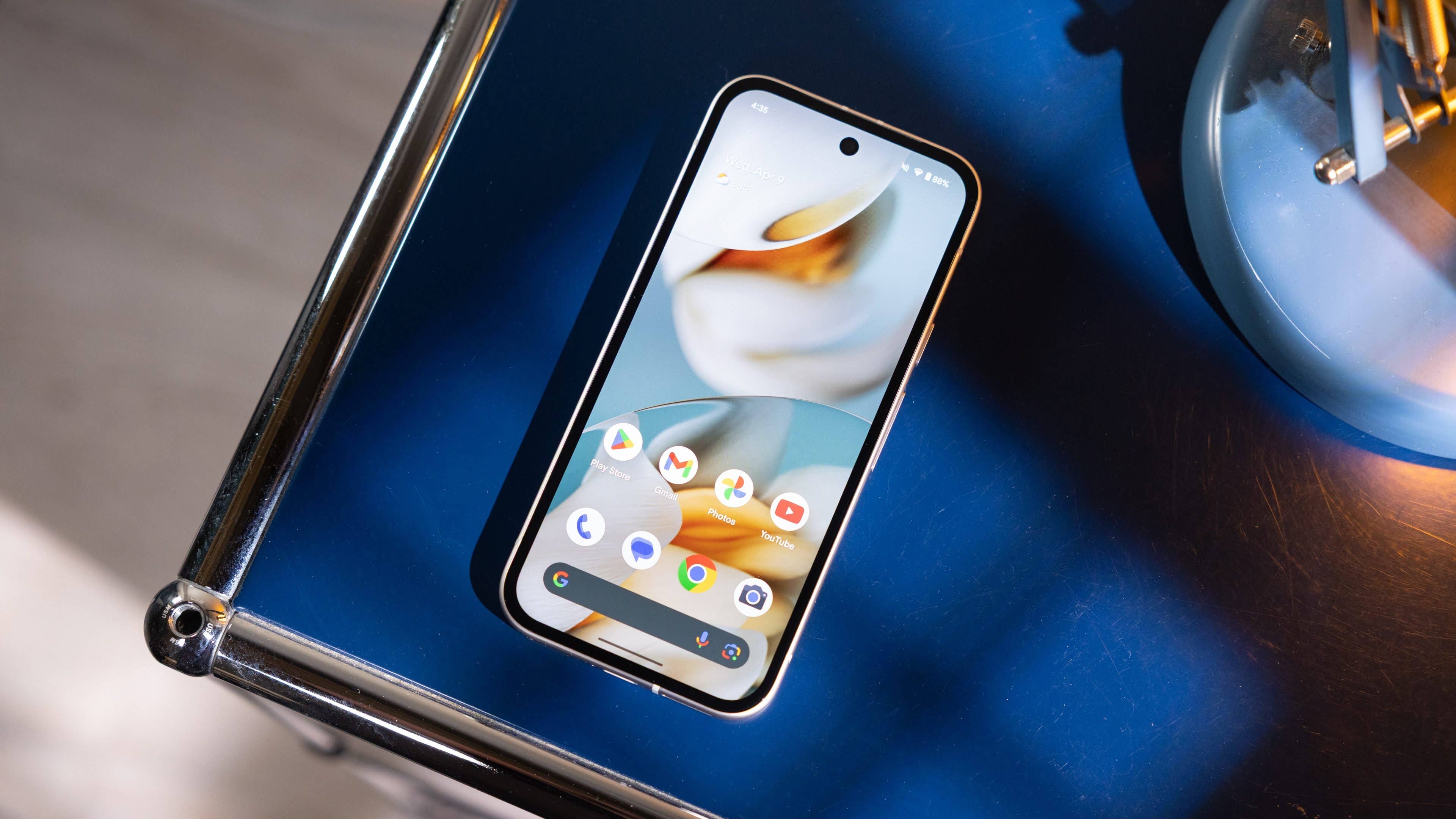 A Google Pixel 9a smartphone displayed on a blue surface next to a blue lamp.