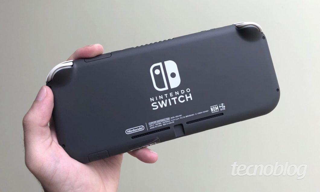 Mão segurando Nintendo Switch Lite com traseira para cima mostrando logotipo do Nintendo Switch ao centro