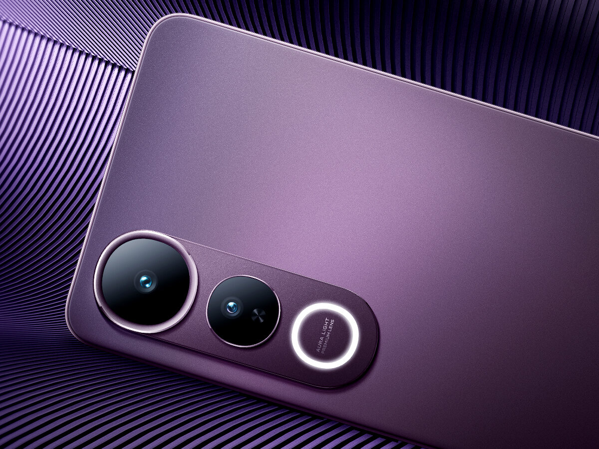 Close-up da parte traseira de um smartphone na cor roxa metálica, posicionado sobre uma superfície roxa com textura ondulada. O destaque está no módulo de câmeras duplas alinhadas verticalmente em uma base oval da mesma cor do aparelho. Abaixo das lentes há um círculo iluminado e, no centro dele, o texto "AURA LIGHT" seguido de "Portrait". As lentes possuem bordas metálicas finas e acabamento reflexivo.