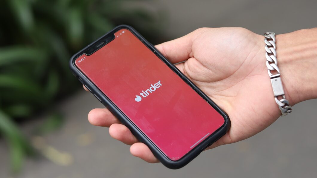 Imagem mostra uma mão segurando um iPhone, com a tela exibindo o logo do Tinder