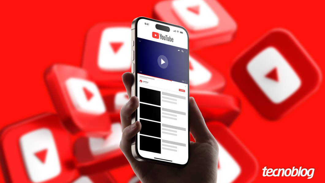 Imagem mostra uma mão segurando um smartphone preto que exibe a interface do aplicativo YouTube. O logo do YouTube, um retângulo branco com um triângulo vermelho apontando para a direita, e a palavra "YouTube" em branco, aparecem na parte superior da tela do smartphone. O fundo da imagem é vermelho com vários logos do YouTube em diferentes tamanhos. Na parte inferior direita, o logotipo do "Tecnoblog" é visível.