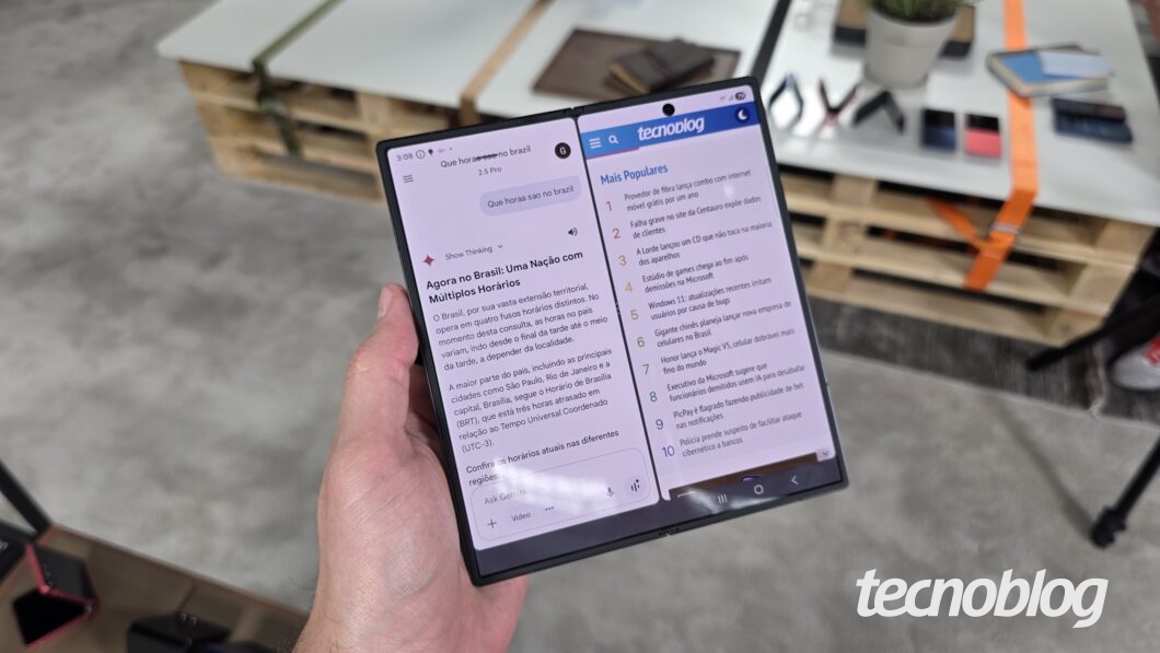 Mão segurando smartphone dobrável aberto, exibindo o Google Gemini e a página do Tecnoblog
