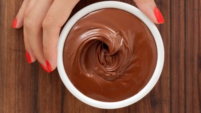 Hand with painted red nails grabbing a chocolate mousse dessert