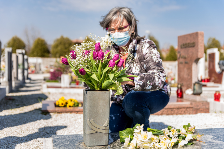 Older lady visiting grave wearing surgical mask