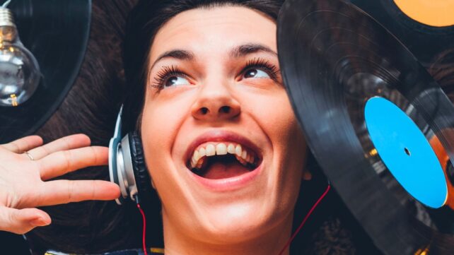 Young woman wearing headphones, surrounded by records