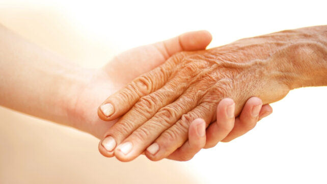 A young-looking hand holding an elderly person's hand