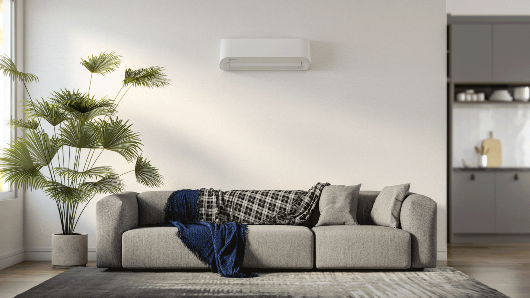 Ar-Condicionado Electrolux pendurado a uma parede branca. Embaixo um sofá e tapete na cor cinza e um vaso de planta ao lado.