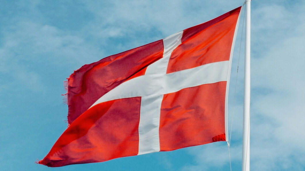 Bandeira da Dinamarca hasteada contra céu azul com nuvens, representando o país 