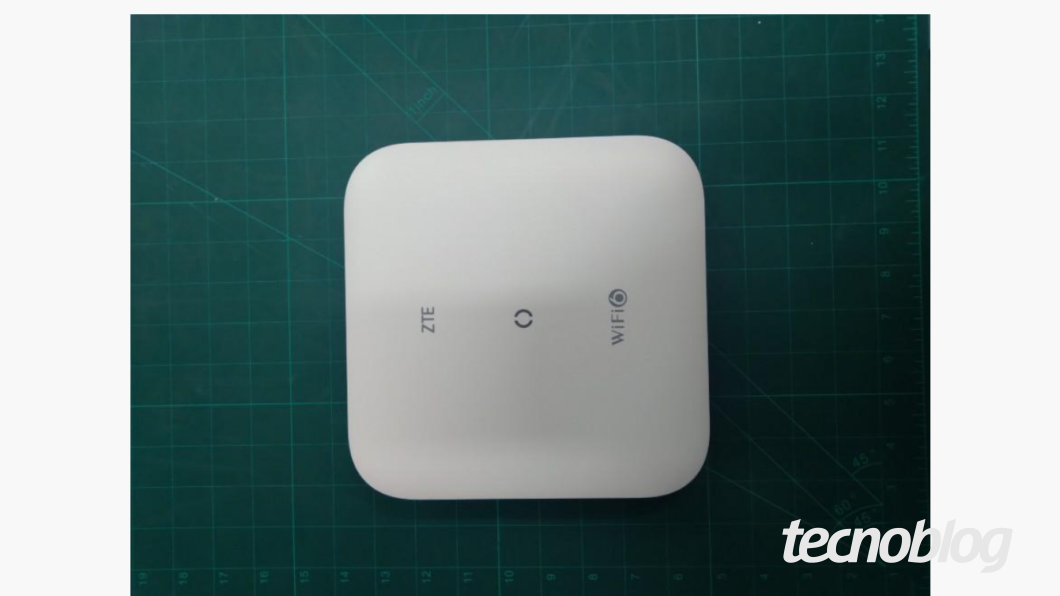 Imagem mostra um modem da ZTE de cor branca, que pode ser preso ao teto, sobre uma superfície verde e quadriculada. Na parte inferior direita, a marca d'água do "tecnoblog" é visível