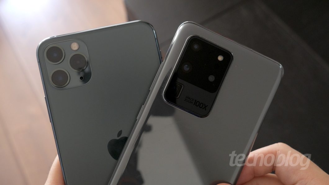 Foto mostra um iPhone 11 Pro Max e Galaxy S20 Ultra sendo segurados nas mãos