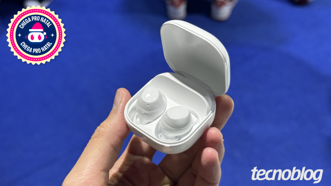 Uma mão segura um estojo de fones de ouvido sem fio de cor branca, que está aberto e revela dois fones também brancos.