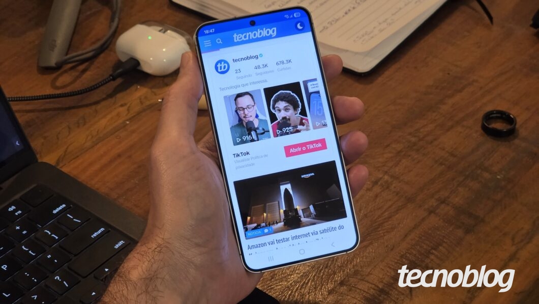 Mão segurando Galaxy S25 com tela ligada mostrando perfil do Tecnoblog no TikTok