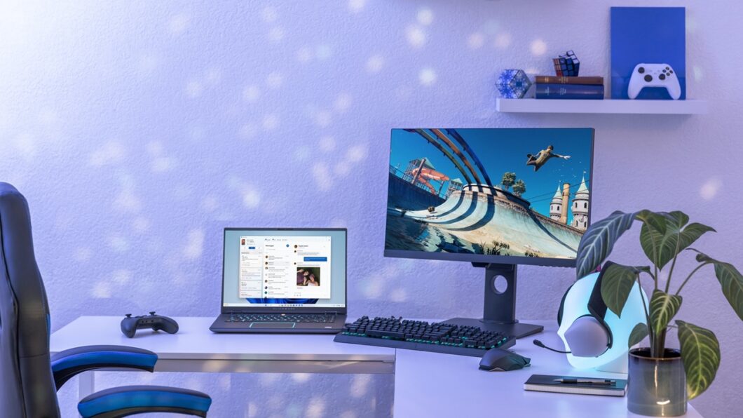 Mesa com notebook rodando Windows e monitor mostrando um jogo