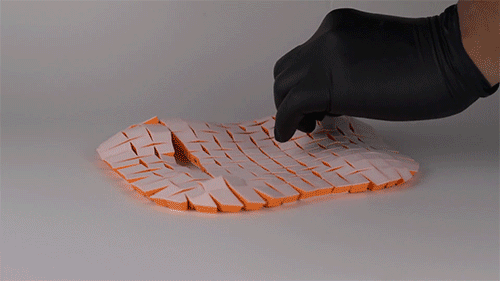 Hand pulls a string and a soft, curved lid-like structure is formed out of interconnected blocks.
