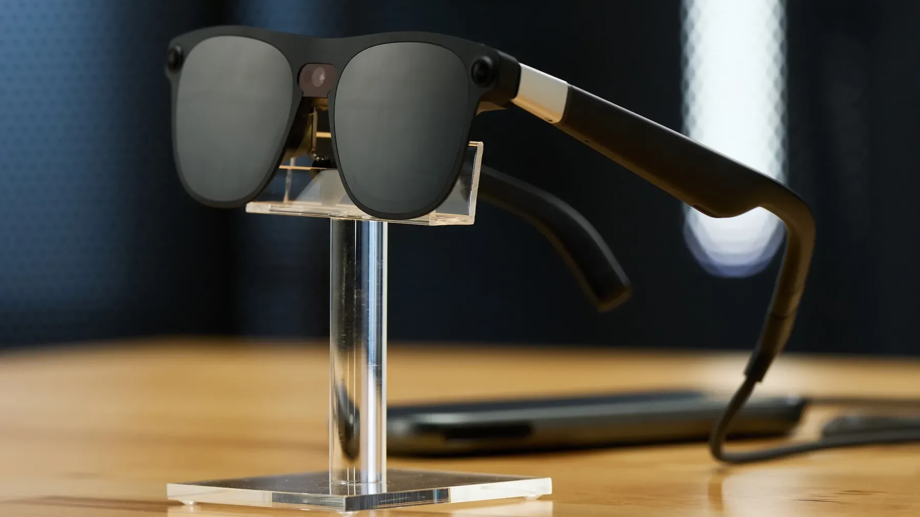 Imagem mostra um novo óculos do Google, de cor preta, exposto sobre uma mesa de madeira