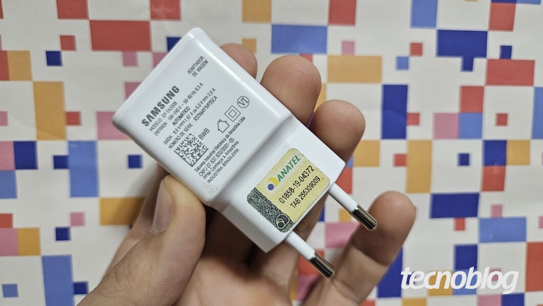 Mão segurando carregador de celular sobre fundo abstrato
