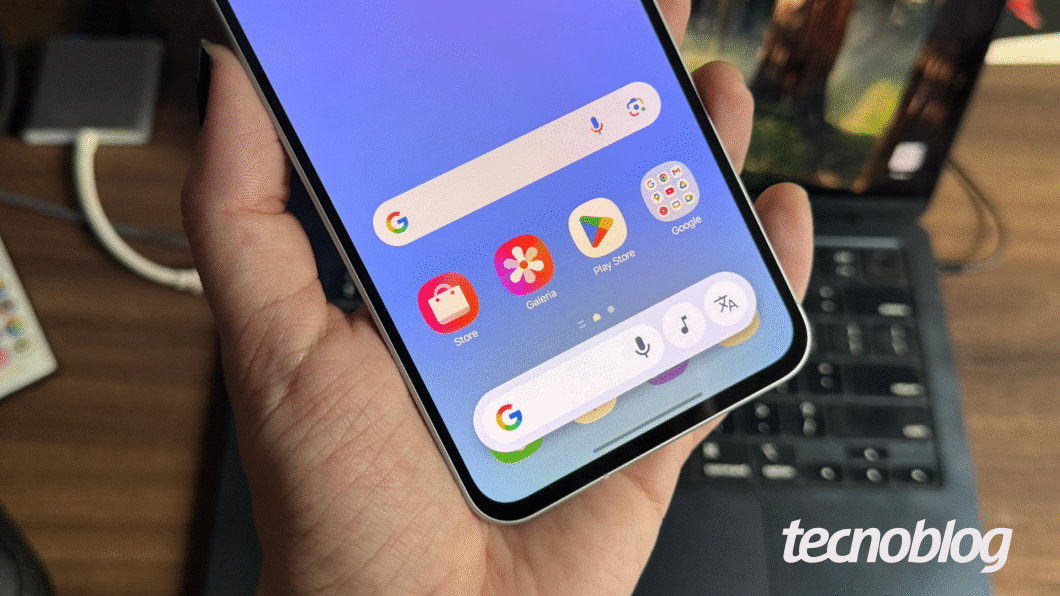 Imagem mostra mão segurando Galaxy A56, exibindo barra flutuante do Google na parte inferior da tela