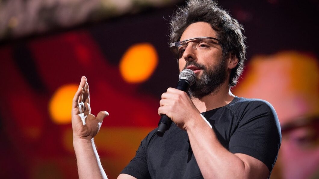 Sergey Brin usando o Google Glass durante apresentação. Ele também segura um microfone