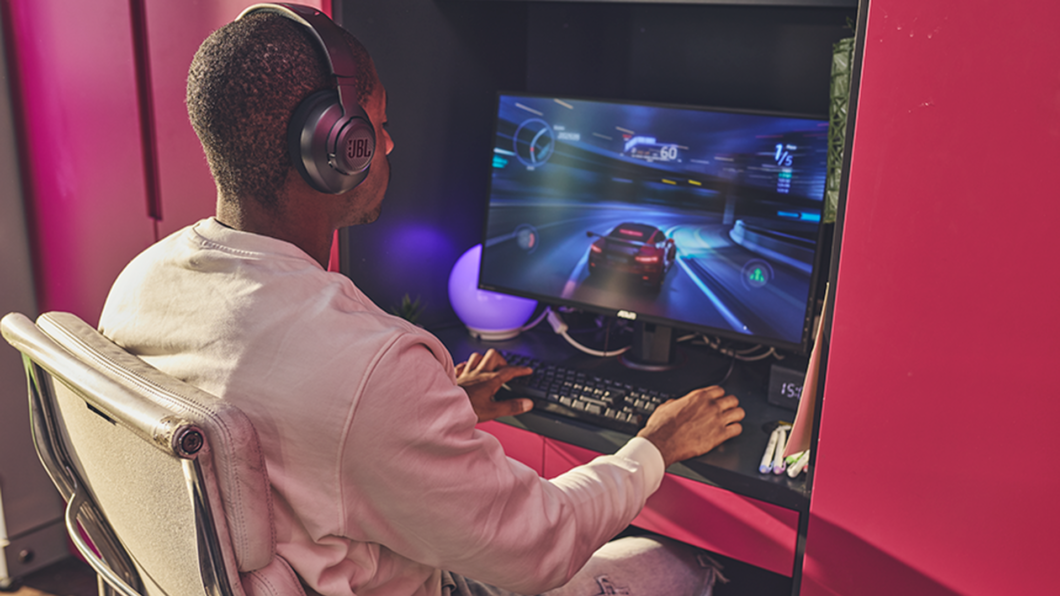 Homem sentado em frente a um computador jogando um jogo de corrida e utilizando o JBL Quantum 100M2