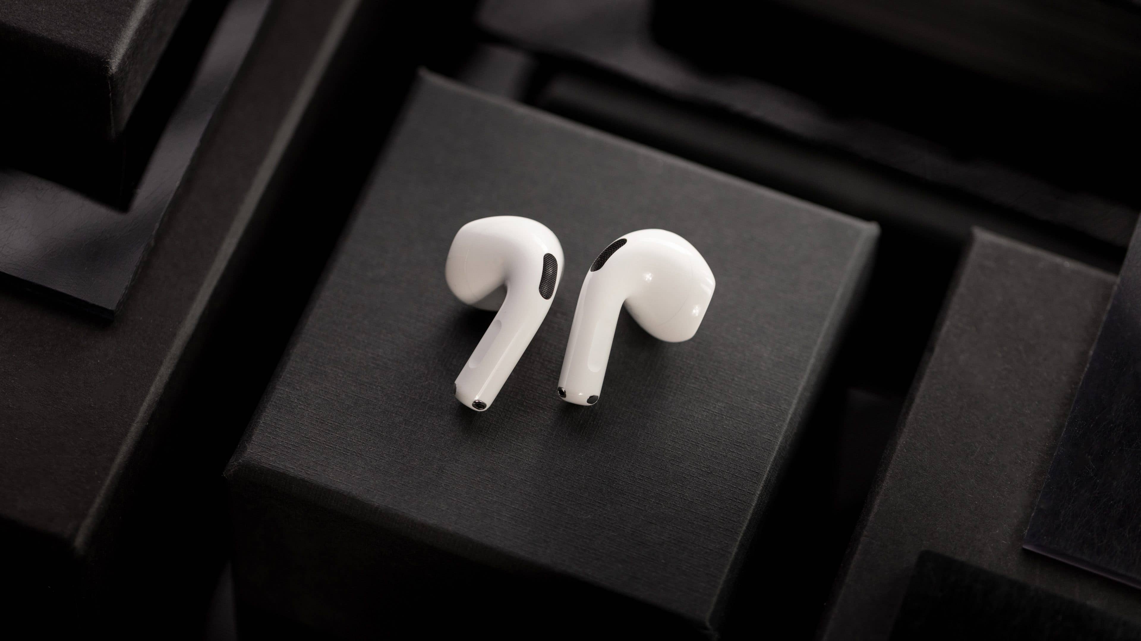 White Apple AirPods on a black background with stacked boxes.