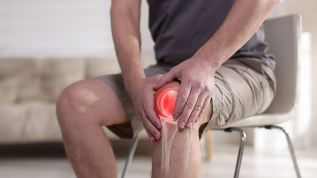 Man holding his inflamed knee, sitting down 