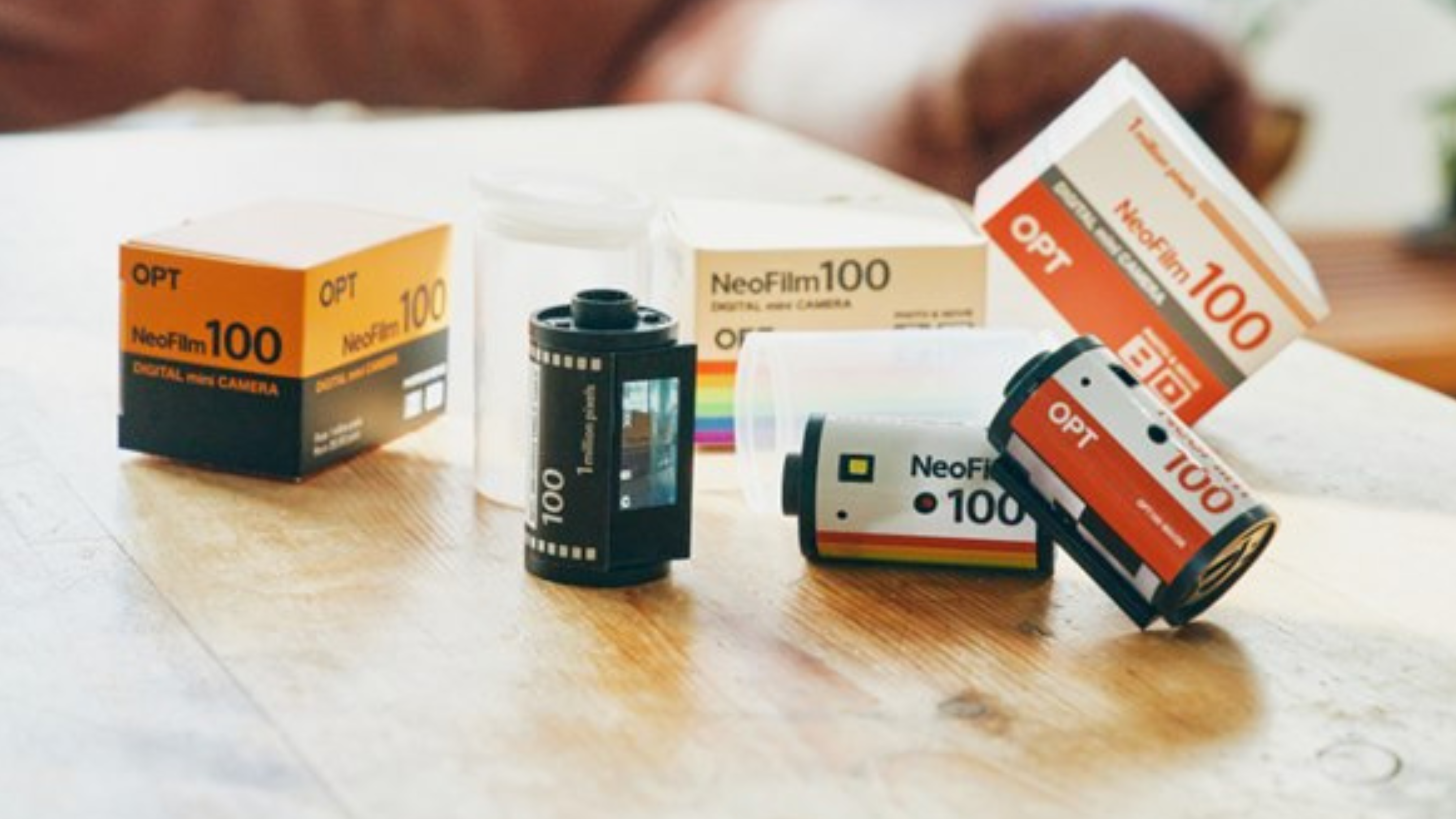 Imagem mostra algumas câmeras OPT100 Neo Film sobre uma mesa de madeira. As câmeras são pequenas e parecem um rolo de filme 35 milímetros.