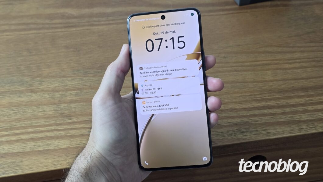 Uma mão segura um smartphone Jovi V50, exibindo a tela de bloqueio com o horário "07:15" e a data "Qui., 29 de mai.". Há um ícone de câmera no canto inferior direito e um recorte em "punch-hole" para a câmera frontal no centro superior da tela. No canto inferior direito, a marca d'água "tecnoblog" é visível.