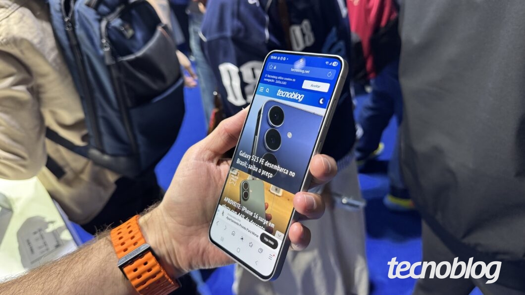 Galaxy S25 FE segurado por uma mão com a tela pra cima e mostrando a home page do Tecnoblog.