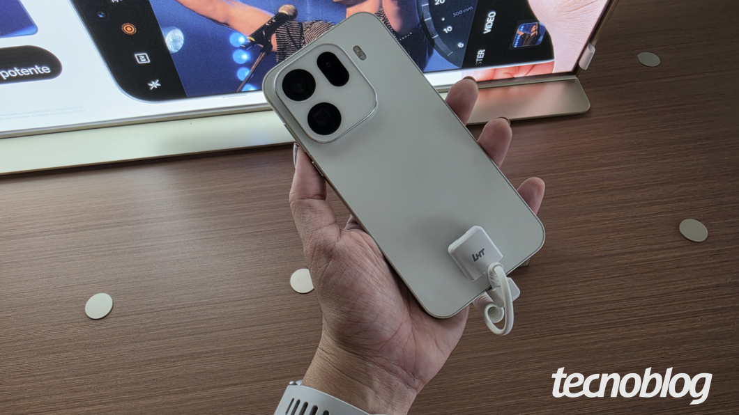 Mão segurando Oppo Find X9 Pro na cor branca sobre mesa de madeira