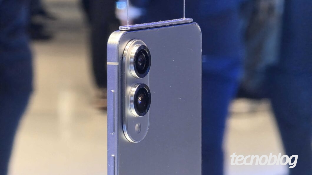 Foto da traseira do smartphone Samsung Galaxy s25 Edge. O foco está no módulo de câmeras, que possui duas lentes posicionadas verticalmente, uma acima da outra, dentro de um contorno metálico ovalado. A carcaça do aparelho é metálica, com acabamento fosco na cor azul ou roxo claro.