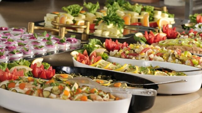 Buffet spread with trays of salads, vegetables, cheese, eggs, and shared serving utensils
