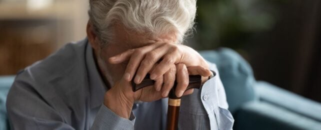 Elderly man resting head on hands holding walking cane
