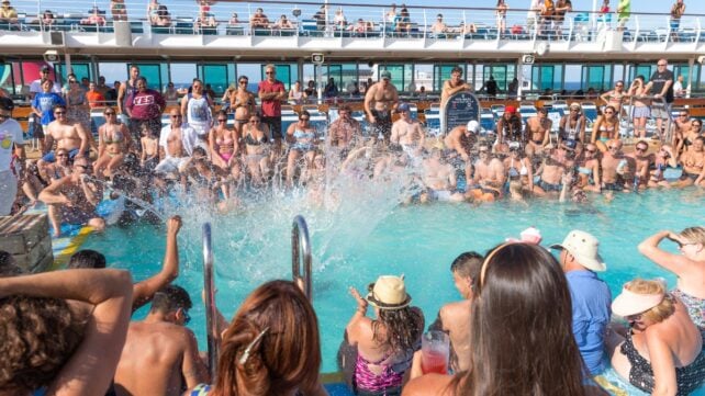 Crowd of passengers gathered around a swimming pool on the deck of a cruise ship