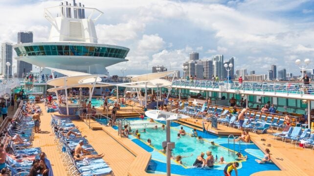 Passengers relaxing around crowded swimming pools and lounge chairs on the deck of a cruise ship