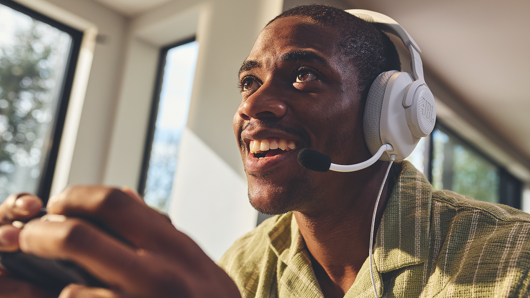 Homem utilizando o JBL Quantum 100M2 na cor branca e segurando um controle de videogame nas mãos.