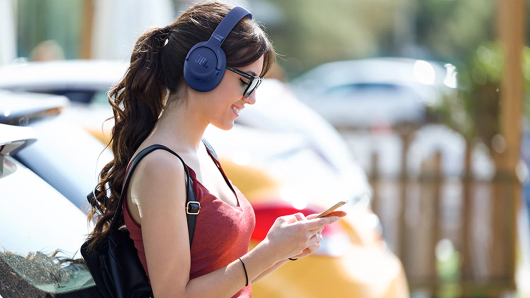 Mulher usando o JBL Tune 780NC e mexendo no celular com as duas mãos