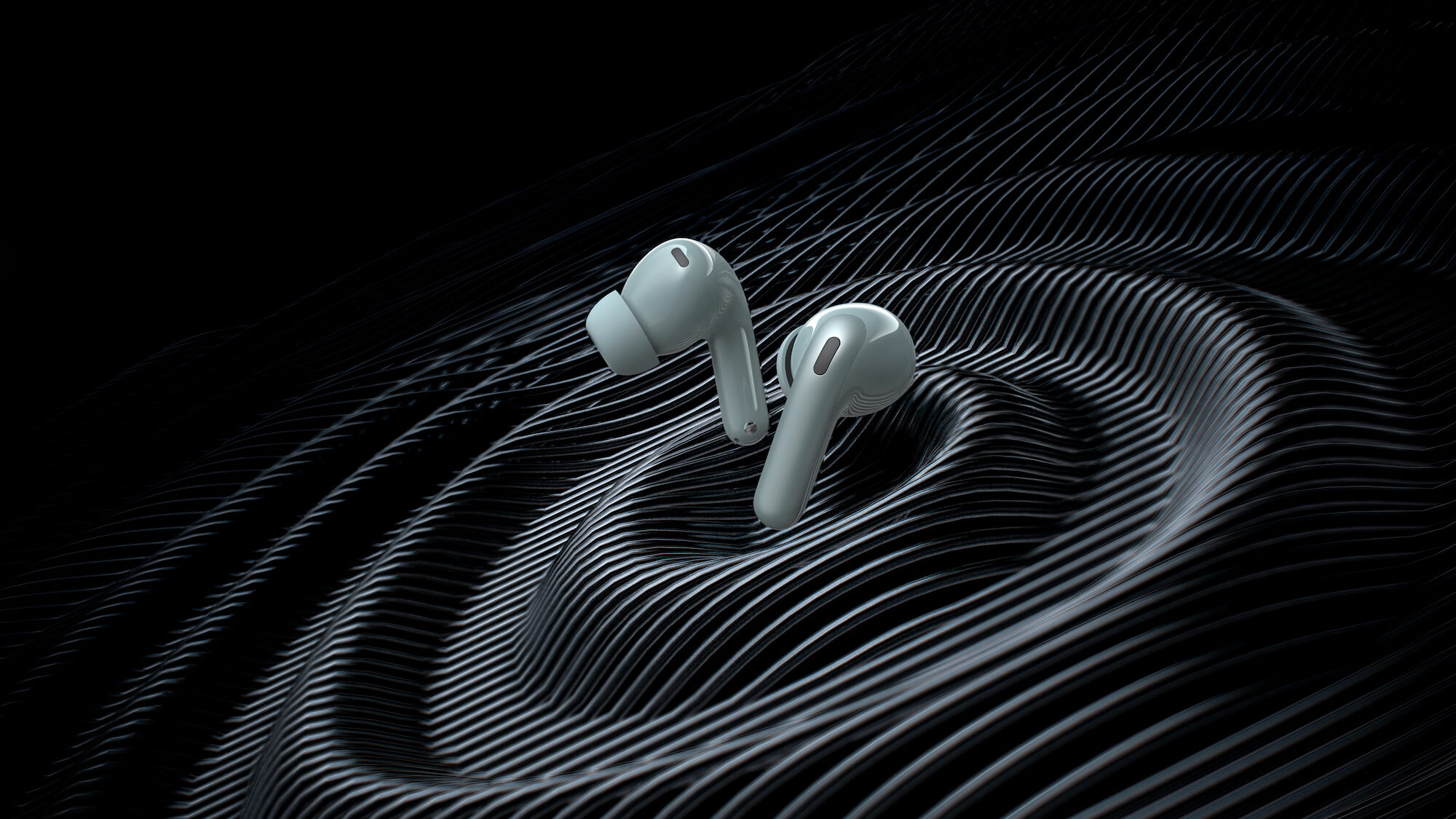 Um par de fones de ouvido sem fio na cor verde-claro flutua centralizado sobre uma superfície abstrata e escura. Os fones possuem design intra-auricular com pontas de silicone e hastes alongadas. A superfície abaixo deles é composta por inúmeras linhas pretas paralelas que formam ondulações circulares e tridimensionais, assemelhando-se a ondas de choque ou ranhuras de um disco de vinil em relevo. O fundo da composição é totalmente preto, criando um forte contraste com o brilho acetinado dos fones e as linhas metálicas da base. A iluminação incide lateralmente, destacando as texturas das ondas.